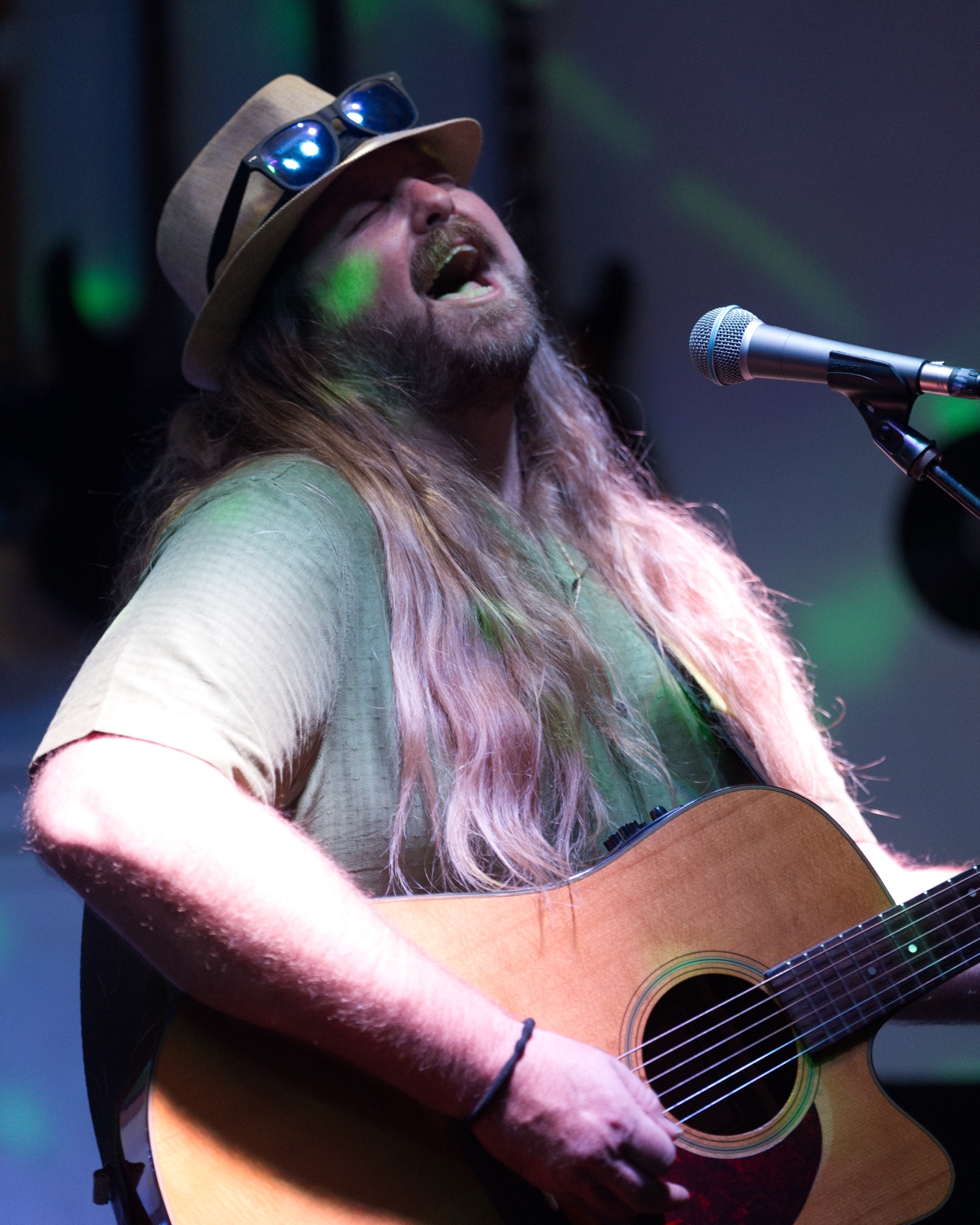 Acoustic singer belting into the mic with eyes closed under green stage lights