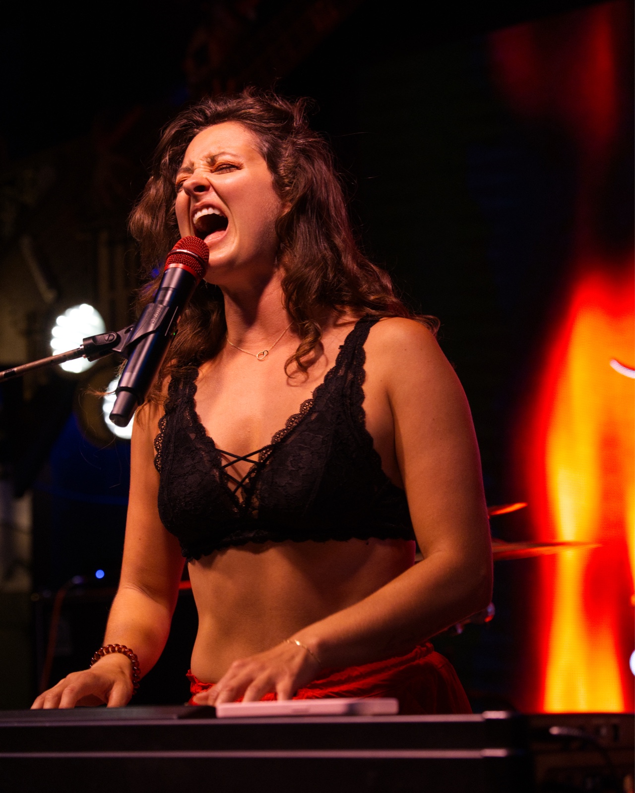 Singer belting passionately into the mic while playing keyboard under red stage light