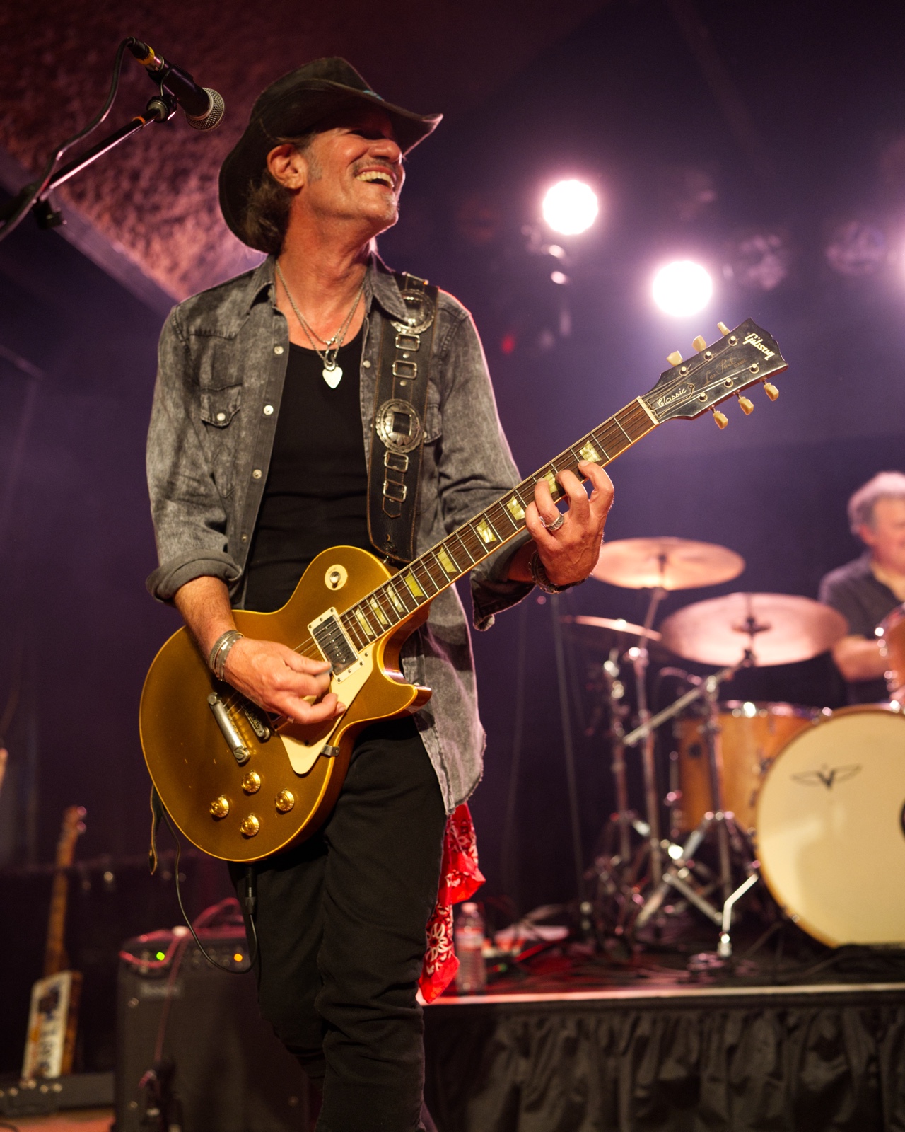 Guitarist laughing while playing a gold Les Paul guitar on stage