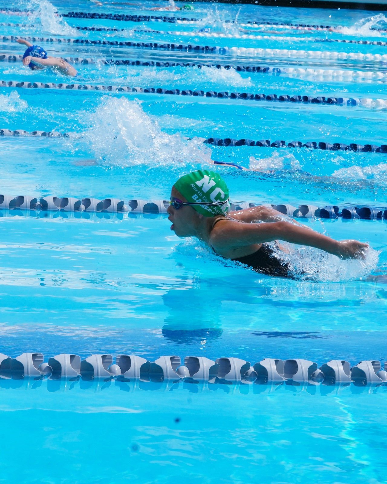Swimmer mid-stroke wearing a green swim cap during a meet